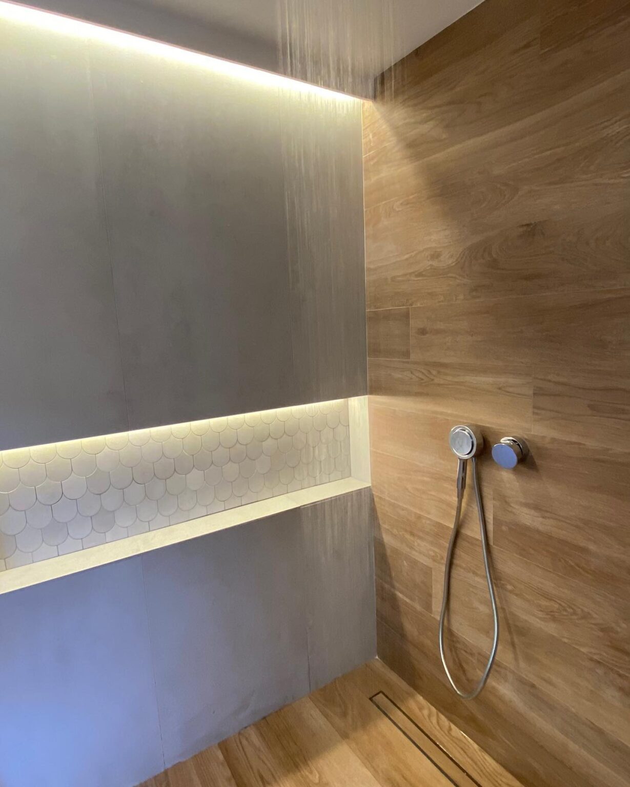 Zona de ducha con alicatado efecto madera, nicho iluminado y grifería empotrada en baño reformado.