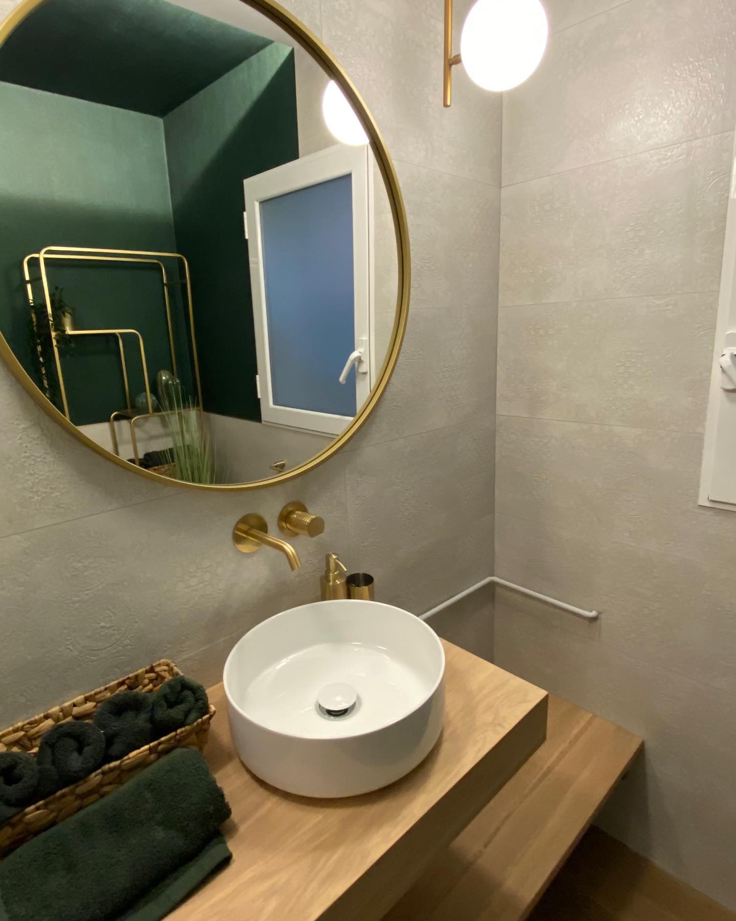 Aseo reformado con lavabo sobre encimera, espejo redondo y grifería dorada en baño moderno.