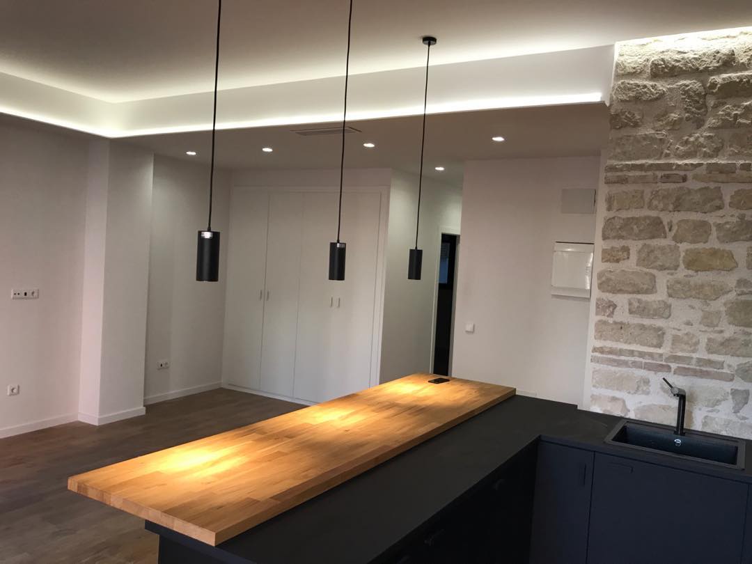 Barra de cocina con encimera de madera e iluminación colgante, en reforma moderna en Alicante.
