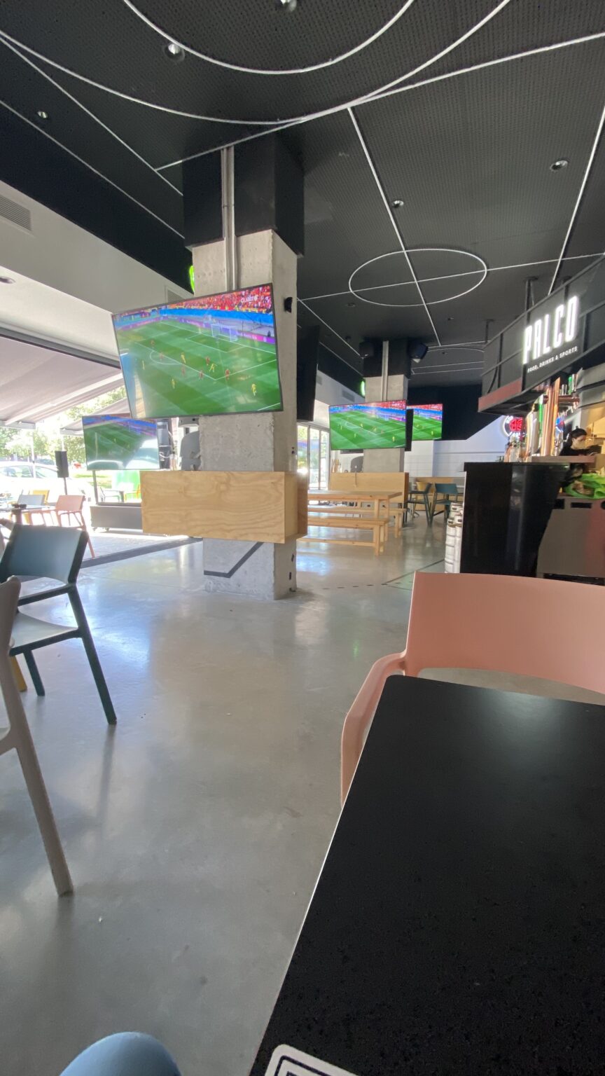 Interior de local de hostelería reformado con zona de mesas, iluminación de techo y pantallas en el salón.