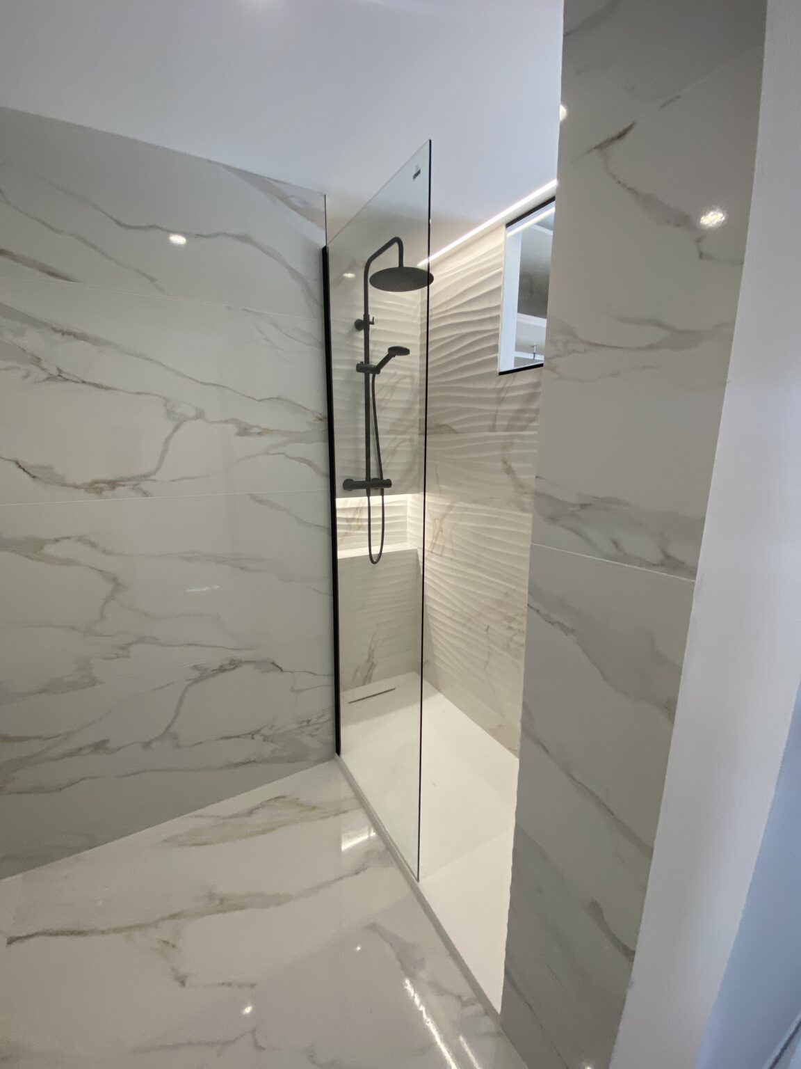 Ducha con mampara de cristal y revestimiento efecto mármol en reforma de baño en Alicante.